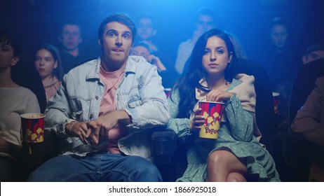 Romantic Couple Watching Film In Cinema. Cheerful Man Hugging Woman In Dark Hall In Slow Motion. Happy Girl Eating Popcorn In Movie Theater.