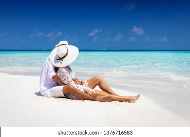 Romantic couple in white summer clothes sits hugging on a tropical beach in the Maldives and enjoys their honeymoon