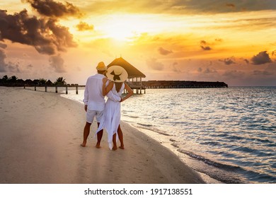 Romantic Couple In White Summer Clothes Looks At The Golden Sunset On A Tropical Beach During Their Holiday Time