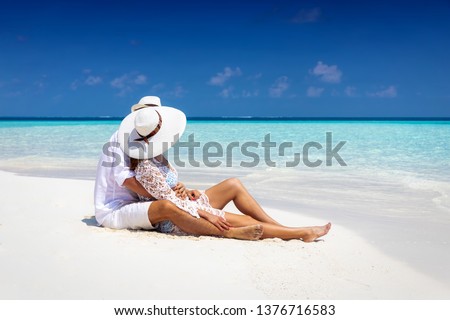 Romantic couple in white summer clothes sits hugging on a tropical beach in the Maldives and enjoys their honeymoon