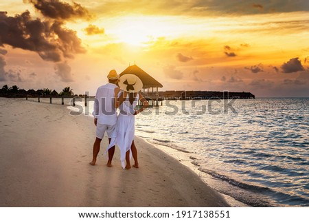 Romantic couple in white summer clothes looks at the golden sunset on a tropical beach during their holiday time