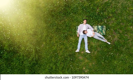 Romantic couple of young people lying on grass in park. They lay on the shoulders of each other and hold hands together. They look happy. View from above.