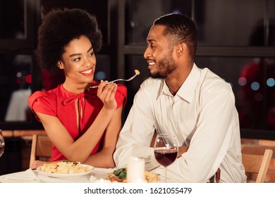 Romantic Date. Attractive Black Woman Feeding Boyfriend During Dinner Celebrating Valentine In Fancy Restaurant