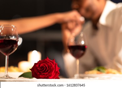 Romantic Date Background. Red Rose Lying On Table, Loving Black Man Kissing Woman's Hand During Dinner In Restaurant. Selective Focus - Powered by Shutterstock