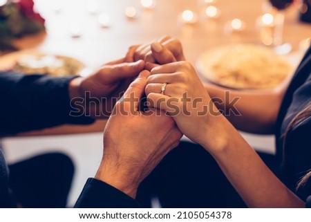 Romantic Date Concept. Selective focus on young loving couple holding hands spending time together at home or cafe, having dinner during date night, candles and food in blurred background