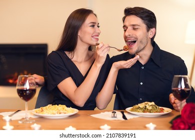 Romantic Date Concept. Smiling Beautiful Girlfriend Feeding Handsome Guy With Pasta. Portrait Of Happy Excited Family Sitting At Table And Eating Meal At Restaurant Or At Home, Drinking Red Wine