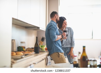 Romantic date at home. Portrait of happy bearded man and his girlfriend holding glasses of wine while talking and laughing - Powered by Shutterstock