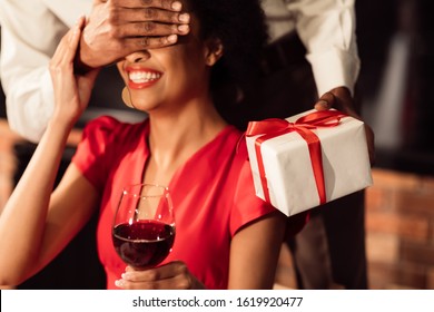 Romantic Date. Unrecognizable African American Boyfriend Covering Girfriend's Eyes Giving Gift Celebrating Valentine's Day In Restaurant. Cropped