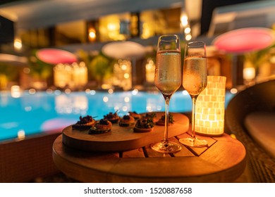 Romantic Decor Candlelight Dinner Table Setup For Party With Champagne Special Dishes And Blurred Out Light Of Pool And House. Luxury Party Or Holiday Event