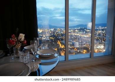 Romantic dining table setting next to window with night city view in a luxury apartment hotel room
