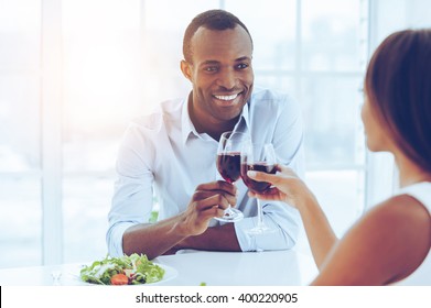 Romantic dinner.. Beautiful young African couple sitting together at the table and holding wineglasses