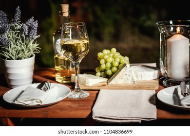 romantic dinner with a glass of wine, and snacks on an old wooden table on a summer evening - Shutterstock ID 1104836699