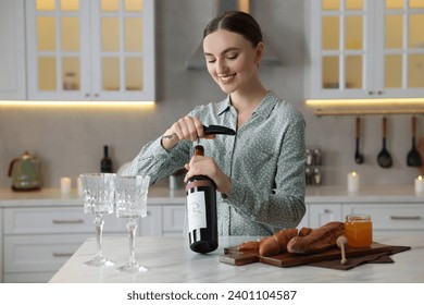 Romantic dinner. Happy woman opening wine bottle with corkscrew at table in kitchen - Powered by Shutterstock