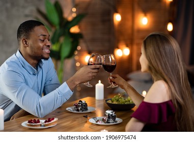 Romantic Dinner At Home. Loving Interracial Couple Dining In Elegant Domestic Atmosphere, Drinking Red Wine, Clinking Glasses And Eating Desserts, Celebrating Valentine's Day Or Anniversary Together