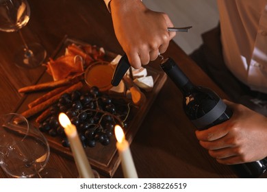 Romantic dinner. Man opening wine bottle with corkscrew at table indoors, above view