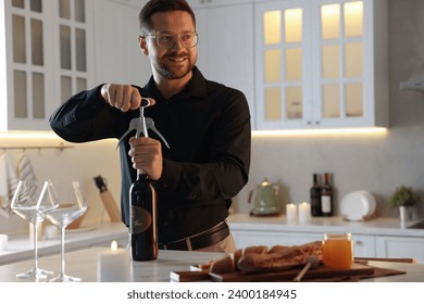 Romantic dinner. Man opening wine bottle with corkscrew at table in kitchen - Powered by Shutterstock