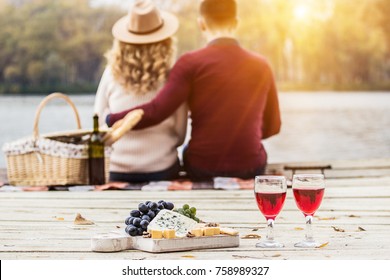 Romantic dinner outdoors. Glasses with red wine, grapes and cheese on wooden board. Young couple having romantic dinner outdoors. Back view man hugging her beautiful girlfriend. Couple in love.