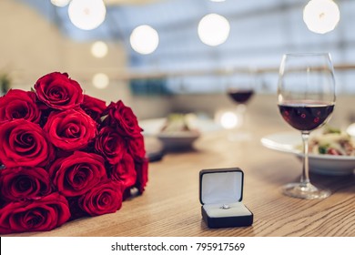 Romantic Dinner Settings. Two Glasses Of Wine, Dishes, Bouquet Of Red Roses And Engagement Ring Are On Table.