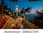 A romantic dinner table set for two, with a couple enjoying a sea view at sunset.

