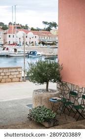 Romantic dinner table set with wine glasses, salad and antipasto appetizer platter next to a pink wall and a potted olive tree, overlooking a scenic sea view in Sali, Croatia.