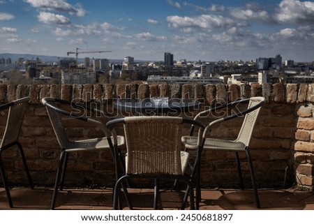 Romantic, dream like view of cafe table by the fortress wall with a city in the distance.