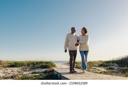 Romantic elderly couple smiling cheerfully while walking down a wooden foot bridge at the beach. Happy senior couple enjoying a refreshing holiday after retirement. - Powered by Shutterstock