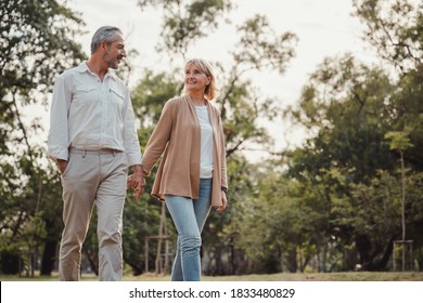 Romantic and elderly healthy lifestyle concept.Senior active caucasian couple holding hands looks happy in the park in the afternoon autumn sunlight,happy anniversary,happily retired with copy space.