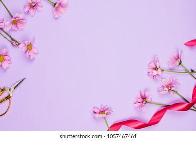 Romantic flatlay frame arrangement with daises, scissors and ribbon, violet background, copyspace