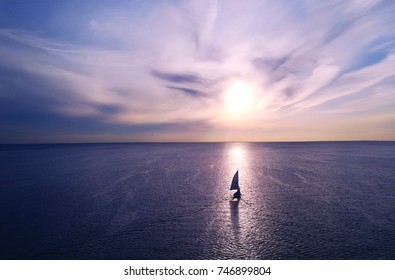 Romantic frame: yacht floating away into the distance towards the horizon in the rays of the setting sun. Purple-pink sunset - Powered by Shutterstock