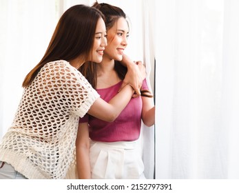 Romantic gay lesbians holding each other smiling. Beautiful sensual Asian homosexual couple intimate moment embracing by window. Portrait of two women hugging with affectionate relationship isolated.