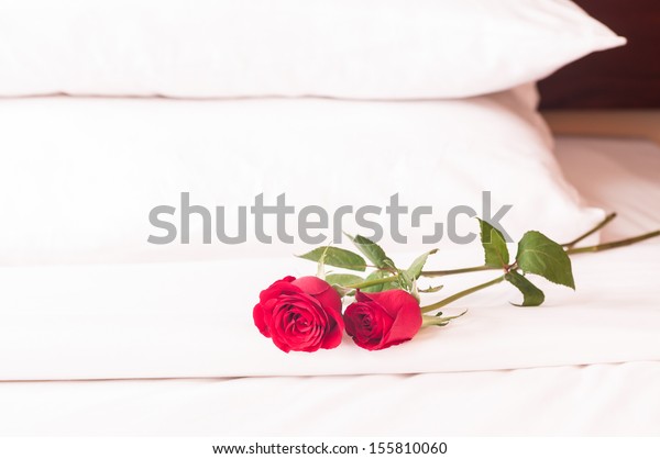 Romantic getaway with red roses on bed and fluffy\
pillows background 