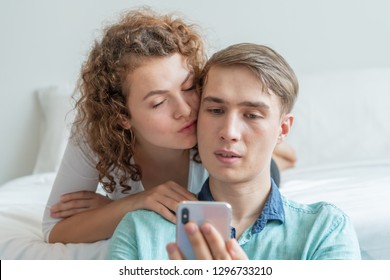 Romantic Happy couple on the bed room checking smart phone media content at home in the morning holiday to planning tour ready for travel booking hotel