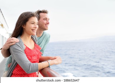 Romantic happy couple on cruise ship on boat travel embracing looking at view. Happy lovers traveling on vacation sailing on open sea ocean enjoying romance. Young Asian woman and Caucasian man.