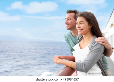 Romantic happy couple on cruise ship on boat travel embracing looking at view. Happy lovers traveling on vacation sailing on open sea ocean enjoying romance. Young Asian woman and Caucasian man.