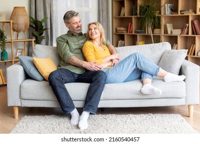 Romantic happy middle aged couple relaxing on couch at home, smiling loving mature spouses resting in cozy living room interior, embracing on sofa, enjoying weekend time together, copy space