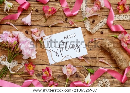 Romantic HELLO SPRING card between pink flowers and vintage ribbons on a wooden table top view. Romantic Valentines day flat lay