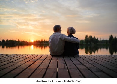 Romantic holiday. Senior loving couple sitting together on lake bank enjoying beautiful sunset. - Powered by Shutterstock