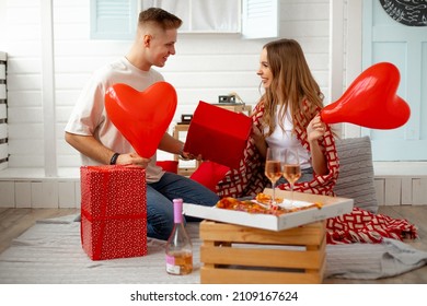 Romantic holiday for young couple is Valentine's Day. They celebrate at home with pizza, wine and red balloons with hearts, exchange gifts and rejoice with each other. Valentine's Day. Tenderness . 