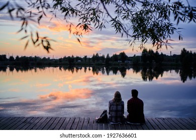 Romantic holiday. Young loving couple sitting together on lake bank enjoying beautiful sunset.