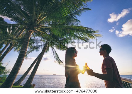 Romantic holidays. Youth and vacation. Young loving couple drinking beer together while resting on the sea beach enjoying sunset.
