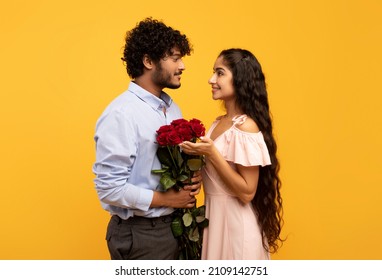 Romantic indian spouses holding bouquet of flowers and looking at each other, loving guy pampering his girlfriend with roses on Valentine's Day, yellow studio background - Powered by Shutterstock