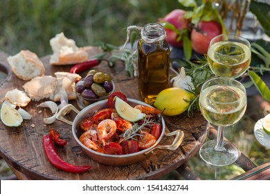 Romantic Italian Lunch Outside Of A Couple: Copper Pan With Delicious And Spicy Fried Shrimps With Herbs And Garlic, Bottle Of Olive Oil, Wine, Bread. Luxury Lifestyle, Gourmet Food.