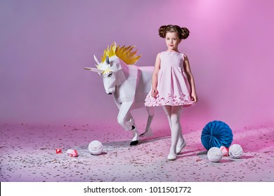 Romantic little girl in beautiful pink dress. Origami and minimalism. Fashion children. Designer collection. White big unicorn origami made of paper.
