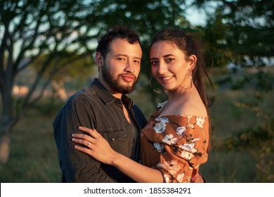 A romantic and lovely latin couple hugging each other in a beautiful sunny day with a dry grass field and a sunset in the background