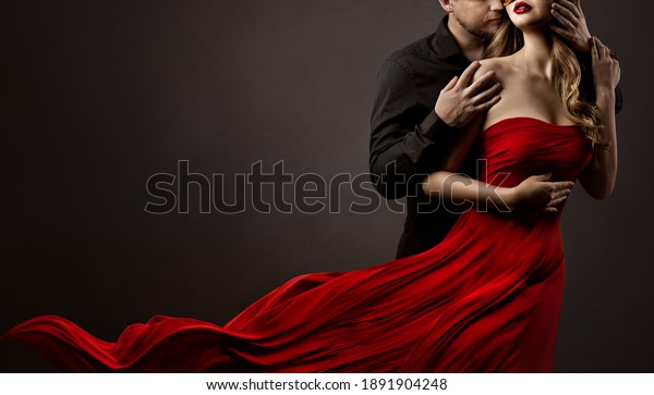 Romantic Lovers Couple Dancing. Man hugging
and kissing beautiful Woman in Silk Red flying Dress. Fashion
Portrait. Studio Black
Background