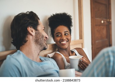 Romantic, loving and happy interracial couple having a cup of coffee on a bed in the morning at home. People in love, smiling in the bedroom with a warm beverage. Happy young man and woman bonding - Powered by Shutterstock