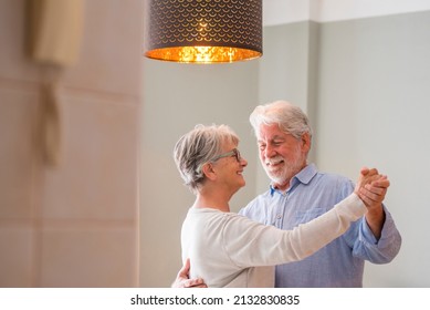 Romantic Loving Senior Couple Holding Hands Enjoying Dancing Together In The Living Room Of House, Elderly Happy Couple Celebrating By Doing Dance At Home. Old Husband And Wife Having Fun Time 