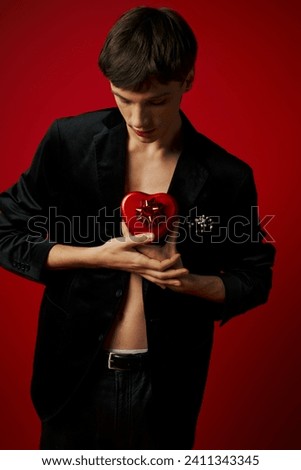 romantic man in velvet blazer holding heart-shaped present on red background, Valentines day