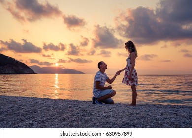 Romantic marriage proposal on the beach at the seaside at sunset over the sea. Young couple in love - Powered by Shutterstock