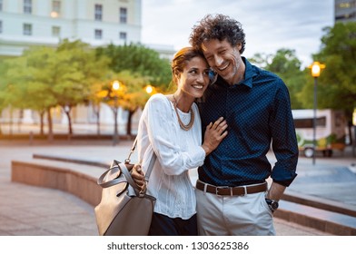 Romantic mature couple enjoying evening walk after office. Cheerful man and beautiful woman embracing while walking on city streets. Handsome man and woman spending evening together outdoors.